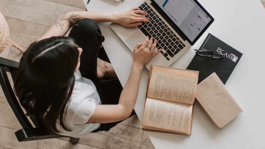 A woman journaling about books while working on a laptop at a desk.