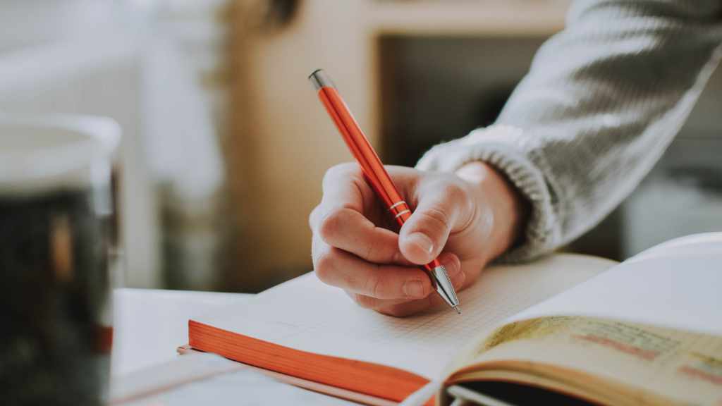Someone about to write in a notebook with an orange pen