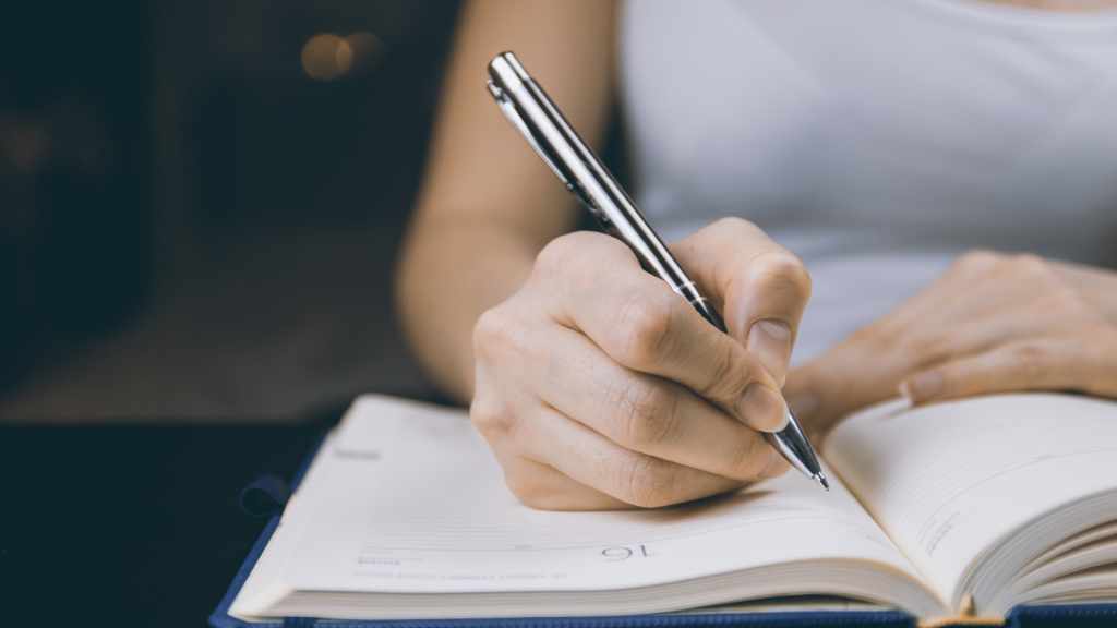 A woman about to write in a journal using a silver pen. Is she journaling with prompts?